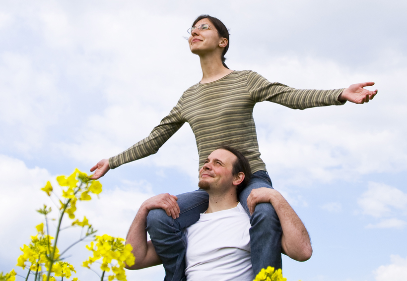Photograph of a woman with arms outstretched, sitting on the shoulders of a man